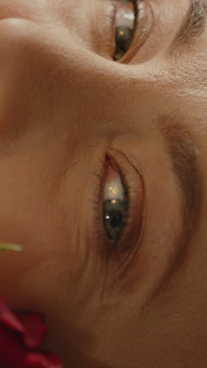 Beautiful vertical macro of a pretty woman's face being caressed by a red rose in slow motion