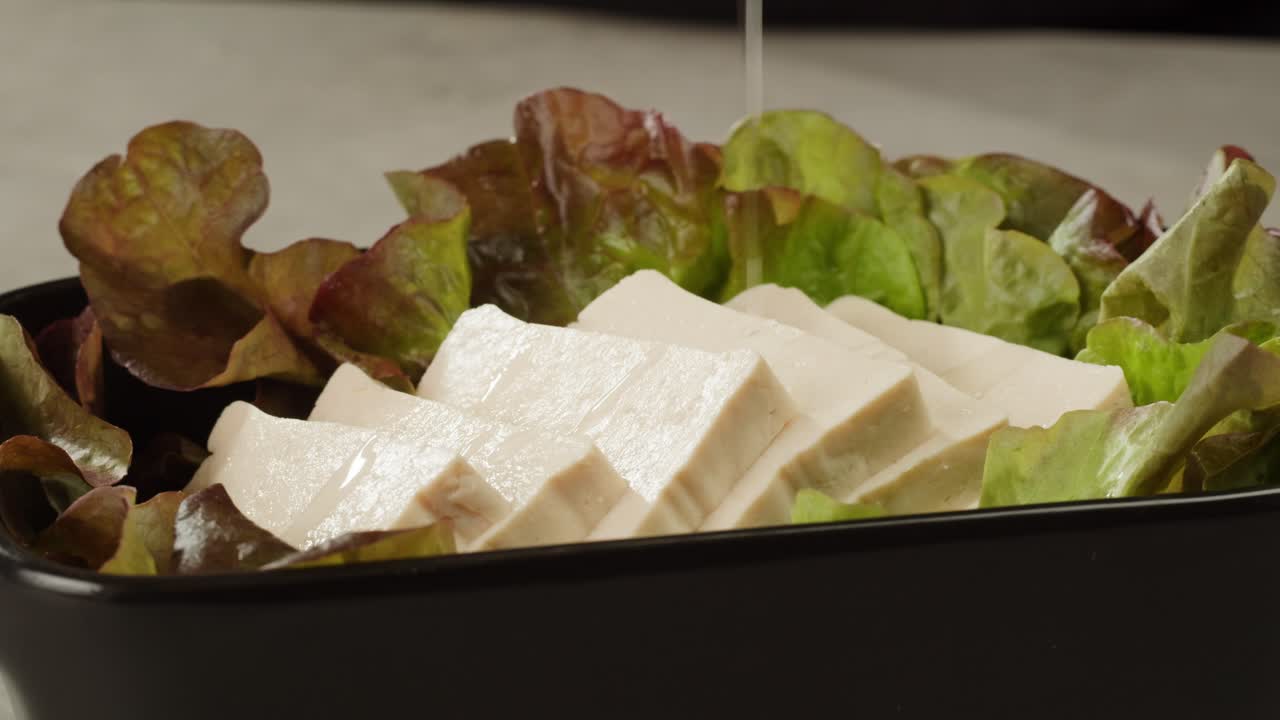 Fried tofu with sesame seeds and spices on cast iron pan, cooking japanese salad. Healthy ingredient for cooking vegan vegetarian diet food. Roasted tofu over black background.