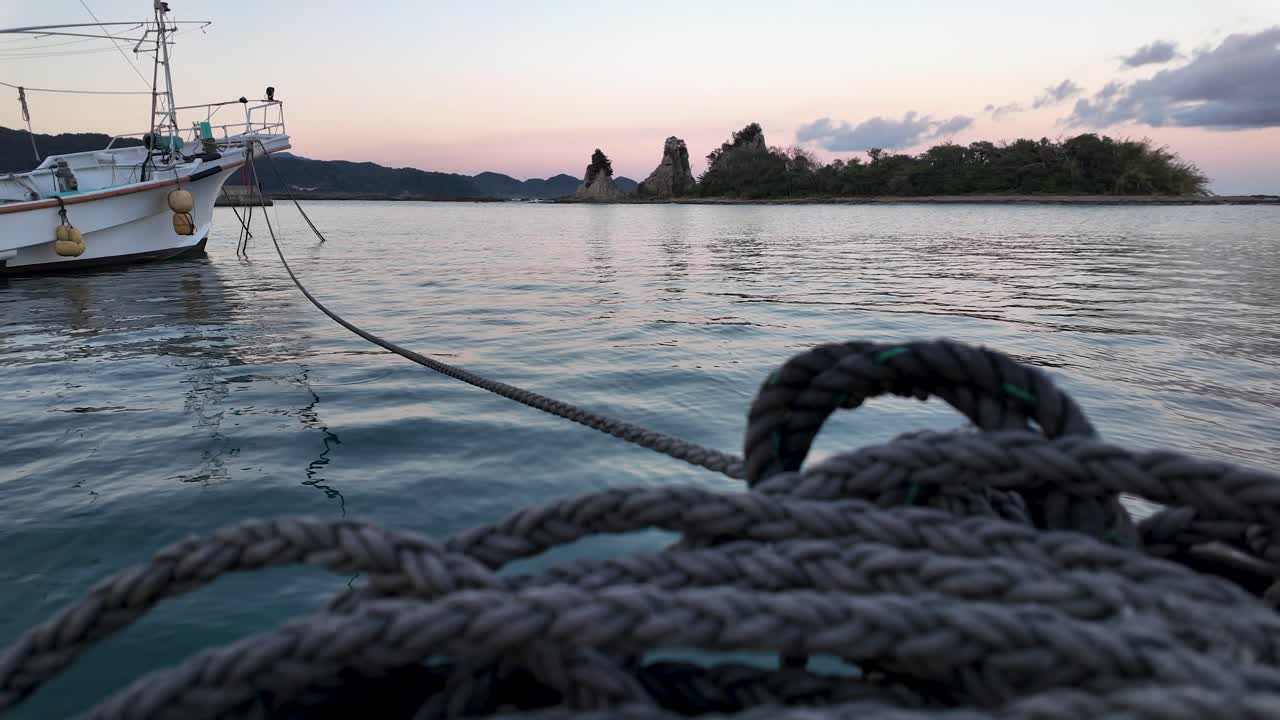 Fishing boat is securely moored with a thick rope at Nachi Harbour, Wakayama, as the golden hour casts a serene glow over the tranquil water