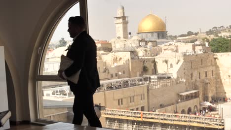 jew with tallit bag walks across loft window with view on jerusalem temple mount