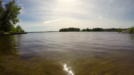 Lakeshore-boreal-forest-time-lapse-low-shot-on-sand-beach-of-waves,-boats-and-clouds-in-Point-du-Bois-Manitoba-Canada-Whiteshell-provincial-park-in-the-Great-Canadian-shield