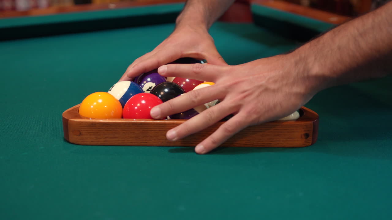 Person Tightens Pool Balls on 8 Ball Triangle Rack with Hands Closeup on the Spot with Solid and Stripped Billiard Balls on Table with Blue Felt or Cloth and Lifts Wooden Triangle