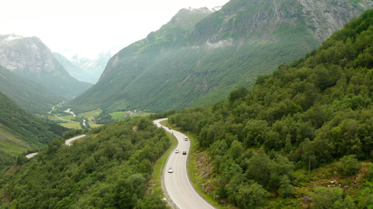 conduciendo autos en una carretera curva en una montaña rodeada de un exuberante bosque verde en stryn, noruega