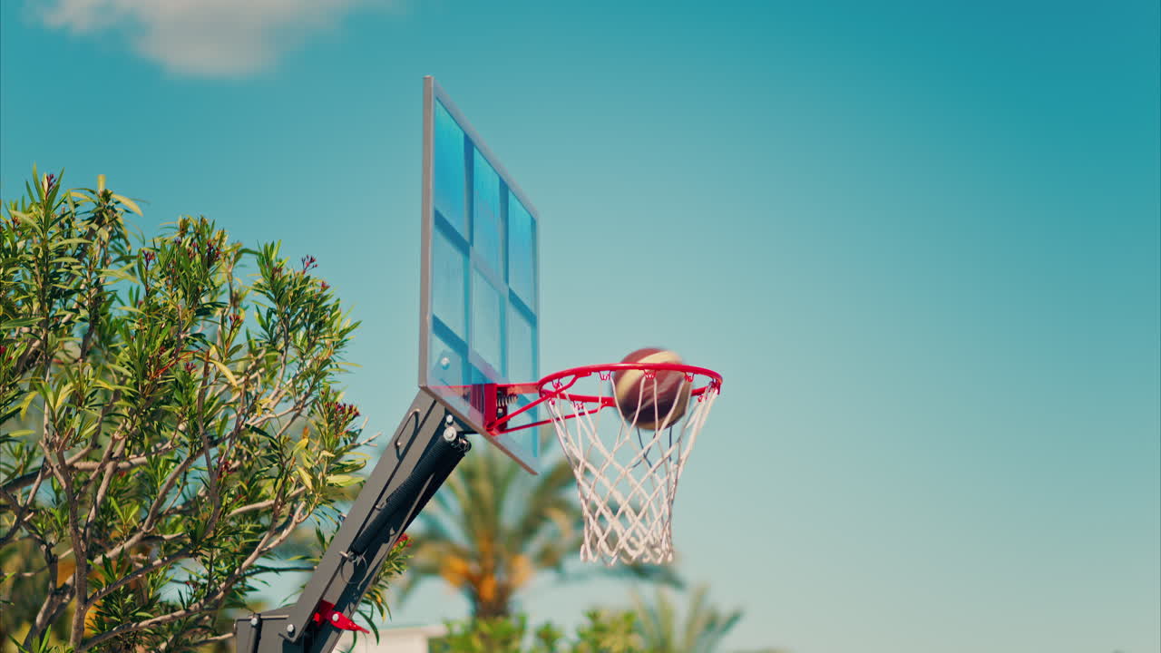 Antibes, France - May 10, 2025: Two basketballs going through the net with palm trees on the background