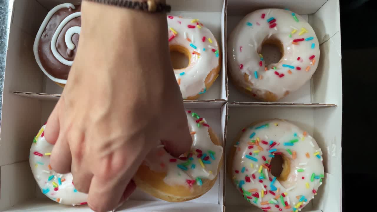 manos femeninas recogen donuts de una caja sobre un fondo negro