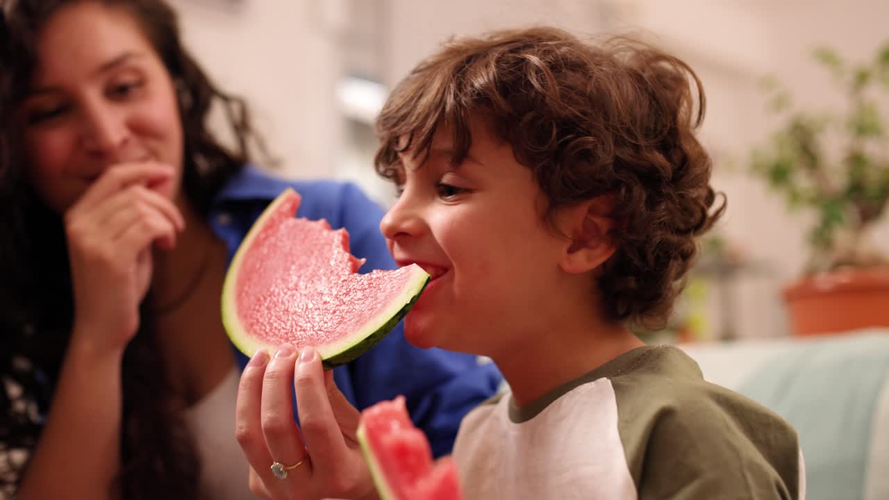 Happy child eating watermelon with mother at home