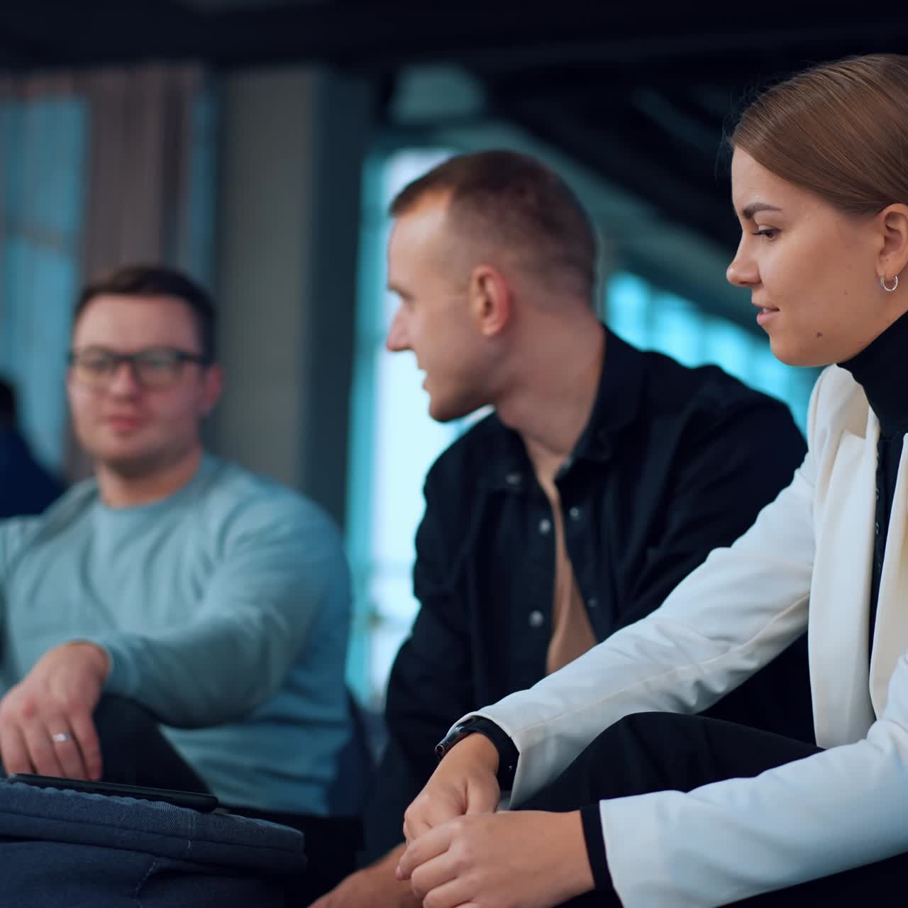 Young people sitting around the table with laptop on. Business colleagues have a discussion of job issues. Communicating team in the modern office. Blurred backdrop
