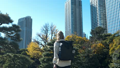 a girl walks through the beautiful pathways of hamarikyu gardens, tokyo, with the modern city buildings in the background.