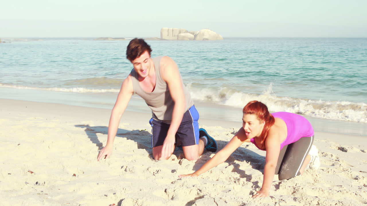 해변 에서 푸시 업 을 하는 미소 짓는 부부