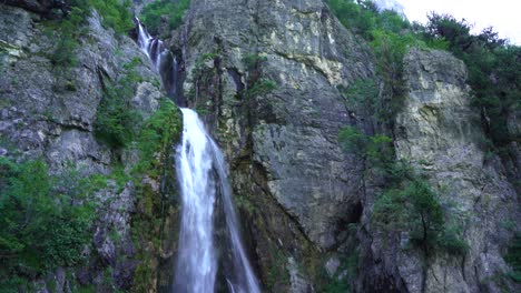 vista ascendente de la hermosa cascada, agua fría y limpia que cae de las montañas rocosas en theth, albania