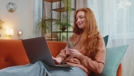mujer joven rica feliz contando dinero en efectivo usando portátil calcular facturas domésticas sentado en el sofá
