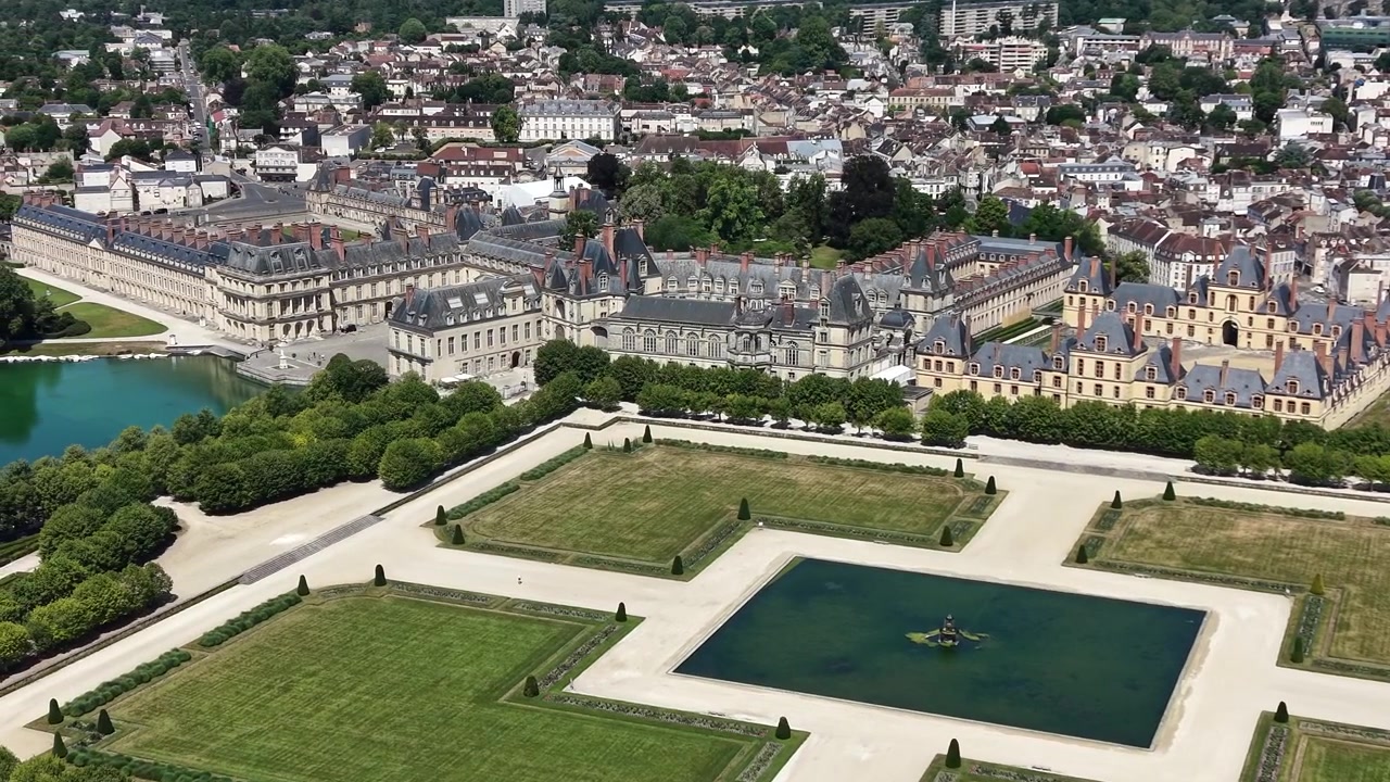 Vista aérea cinematográfica con dron del Castillo de Fontainebleau, que muestra el histórico palacio real, el Gran Parterre con su estanque ornamental reflectante y la ciudad circundante de Fontainebleau, Francia