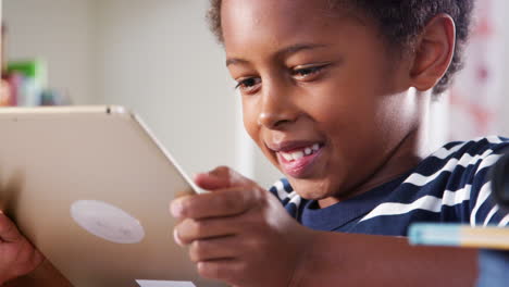 young boy sitting at desk in bedroom playing game on digital tablet