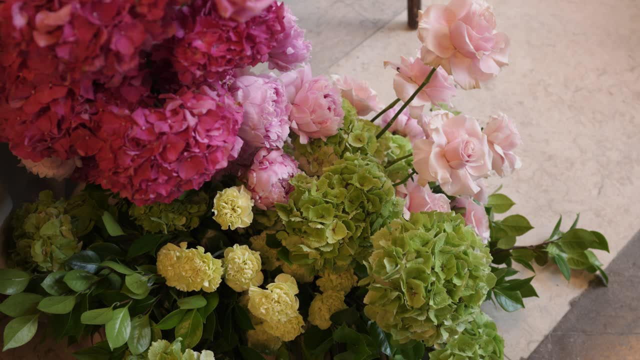 Close up of a colorful floral arrangement featuring hydrangeas and roses in pink, green, and yellow shades