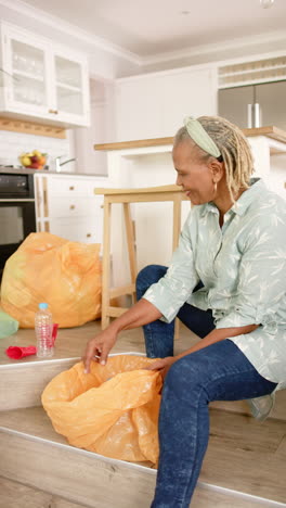 vertical video: a senior african american woman sorting recycling at home