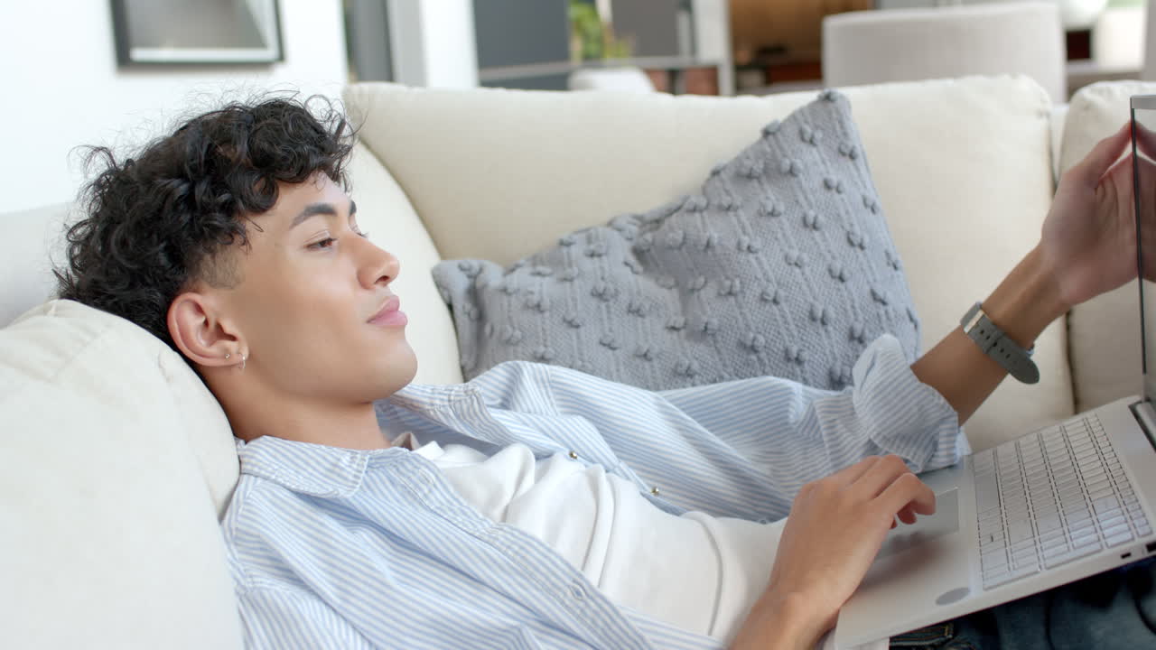 Relaxing on couch, teenage boy using laptop and smiling at home