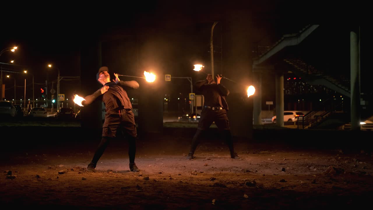 Two fire show artists spin fireballs under the bridge at night. Bokeh on the background. Night performance