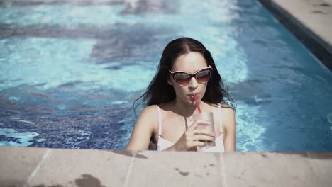 una mujer disfrutando de una copa junto a la piscina.