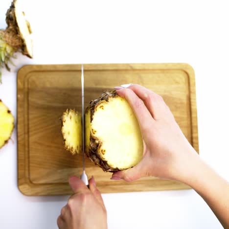 tropical fruit on a board. female's hands cleaning fresh pineapple with a knife on a cutting board. top view.