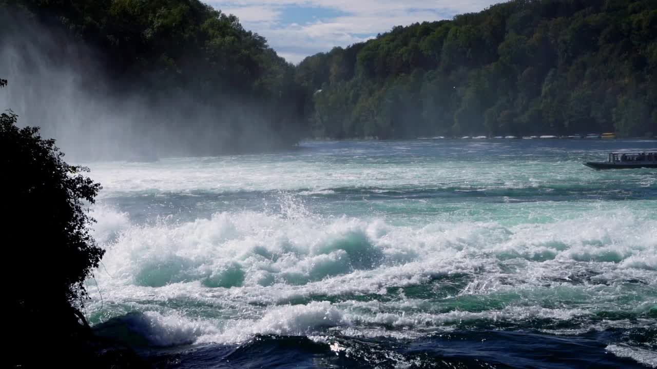 Pan over famous waterfall Rheinfall in Switzerland (slow motion), river rapids, foam and spray, boat approaching waterfall