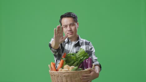 hombre sosteniendo una canasta de verduras con un gesto de parada