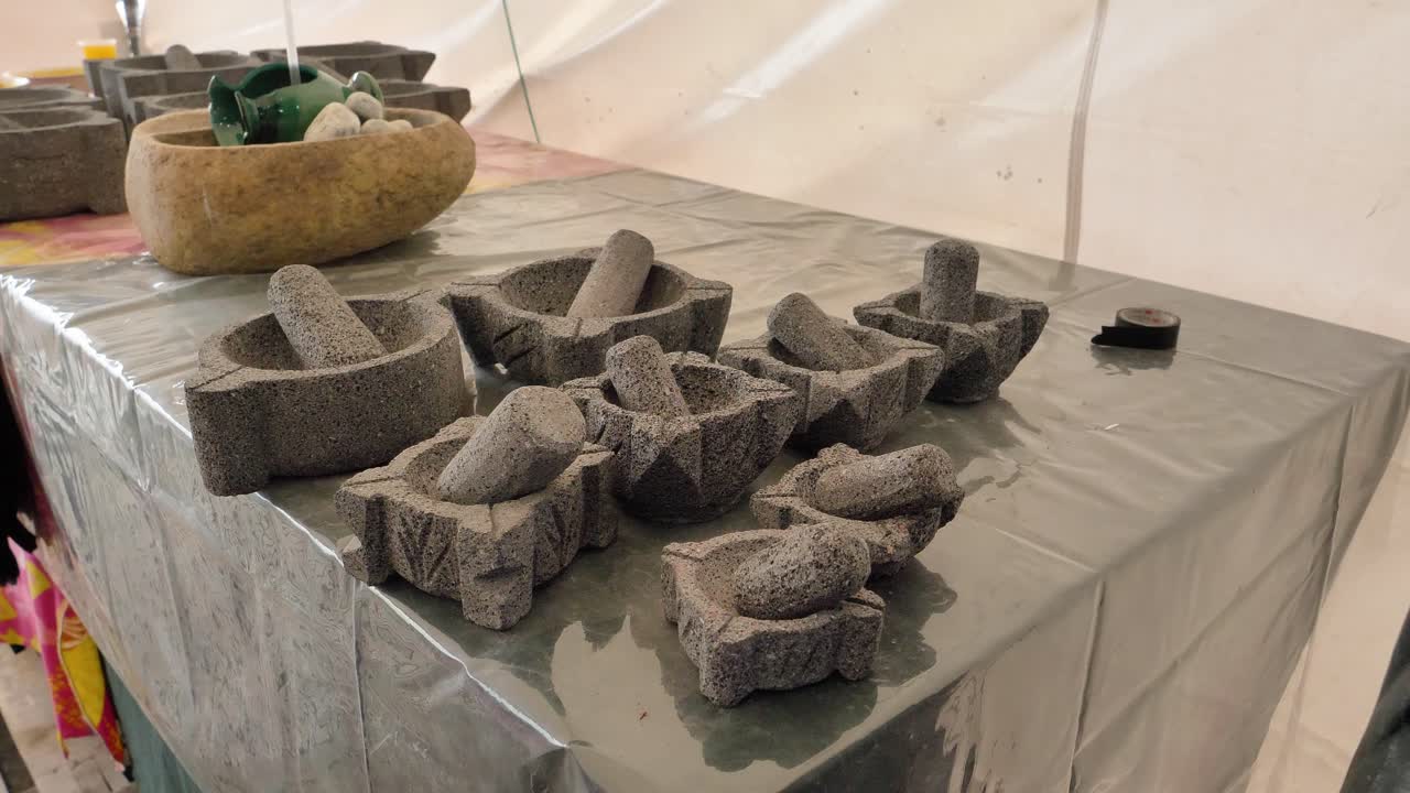 Plan panoramique de mortiers et pilons en pierre faits à la main exposés sur un stand d'artisan dans un marché couvert en Équateur.
