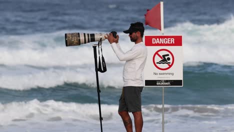 man with camera photographs ocean near warning flag