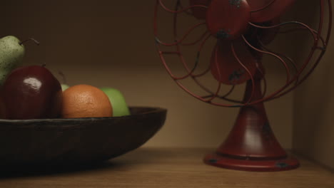 tiro deslizante de un ventilador retro vintage y un tazón de frutas, peras, naranjas, manzanas en un estante