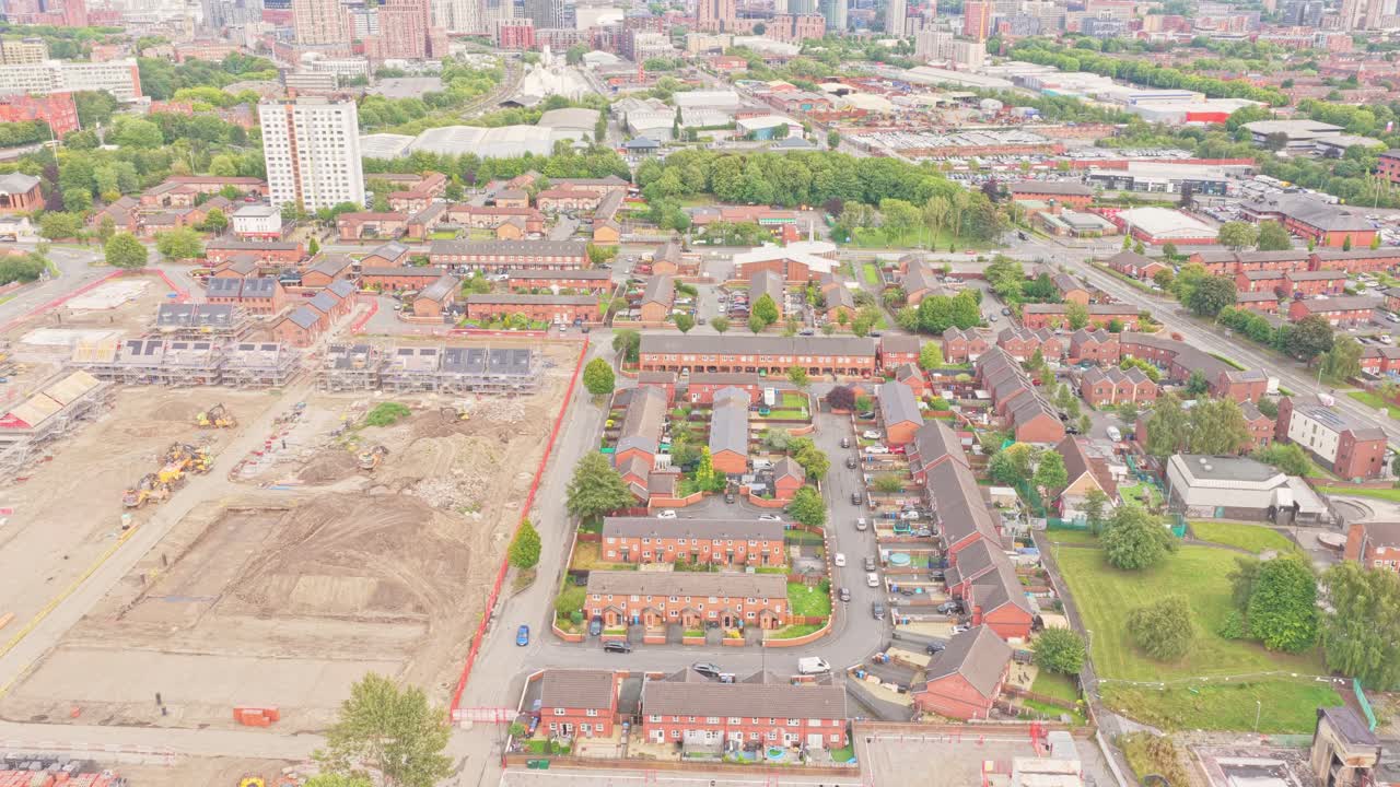 Residential neighborhood in Salford is bordered by an active construction site and framed by the distant city skyline, captured in a descending aerial drone shot
