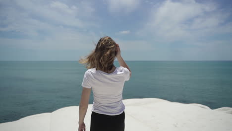 woman on white rock cliff scala dei turchi with view of turquoise blue sea in sicily