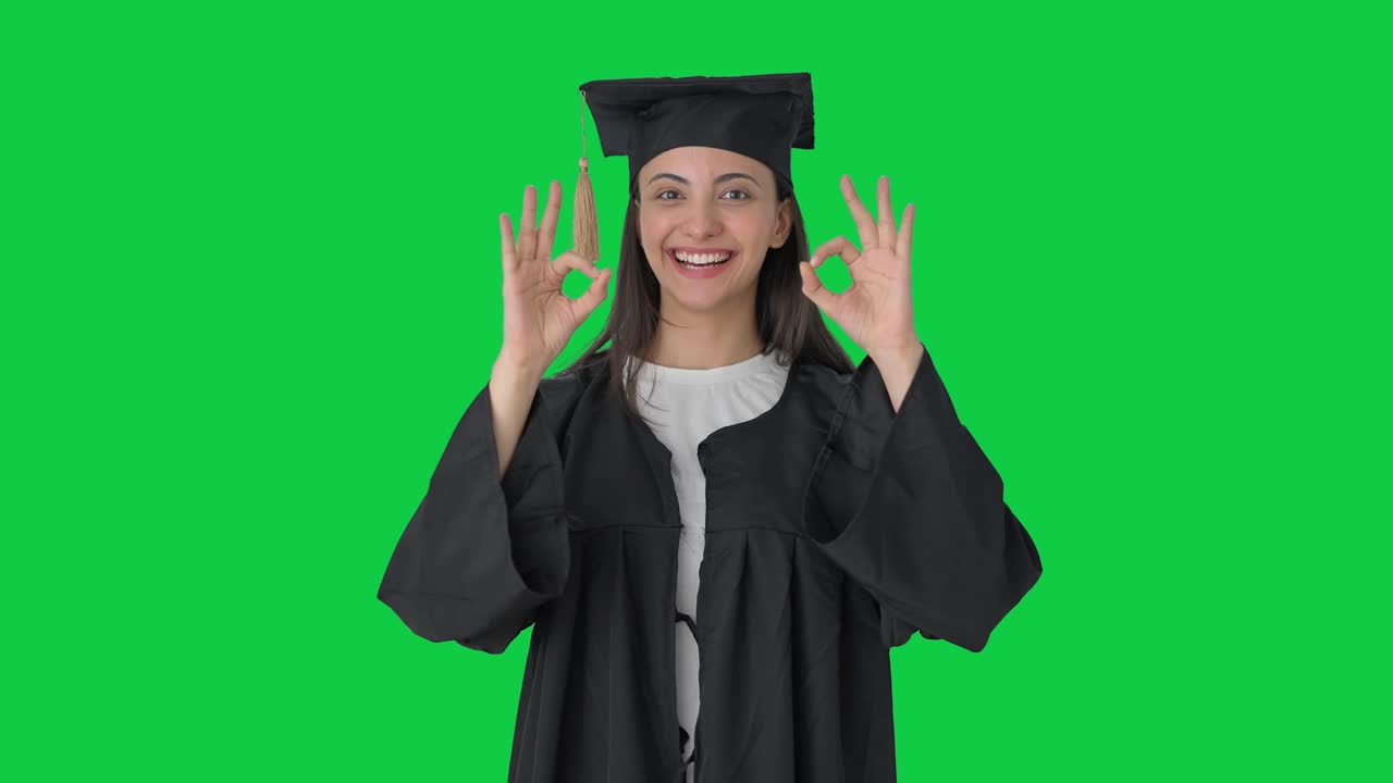 Felice ragazza indiana laureata che mostra il segno dell'okay su green screen