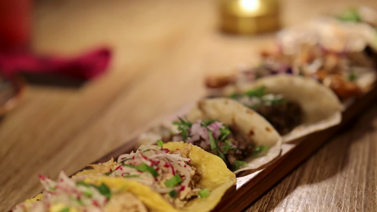 A close-up view of assorted tacos on a wooden table, illuminated by warm candlelight, creating a cozy dining atmosphere