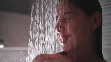 happy woman enjoys water sprays in shower closeup. satisfied lady smiles standing in hot clear flow in bathroom. recreation during bathing time