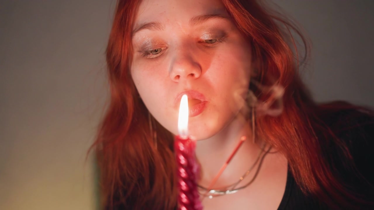 Blond kvinne utfører innendørs seremoni. Rødhåret kvinne fokuserer midt i flimrende stearinlysglød. Kvinne med flammende hår utfører et mystisk innendørs ritual under varmt stearinlys med fokusert intensjon.