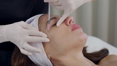 cosmetologist injects botox on the patient’s eyebrow and forehead