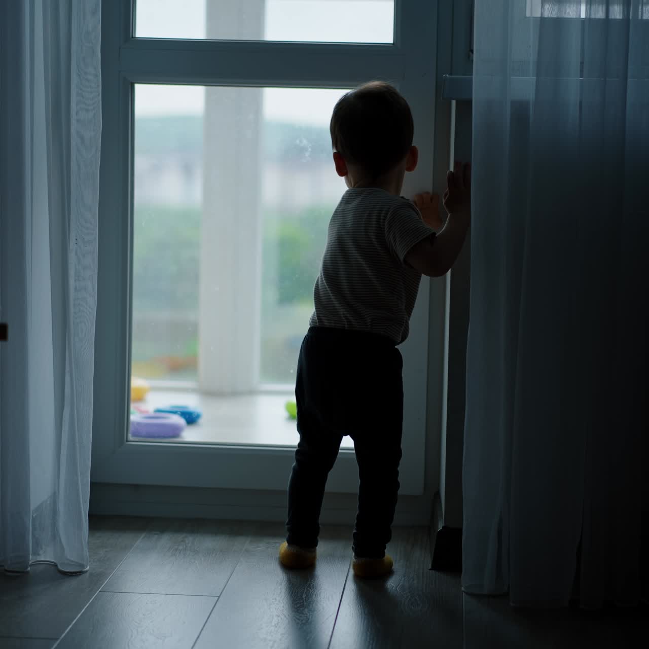 Little baby runs up to a balcony door and closes it. Then opens again and walks happily to a balcony