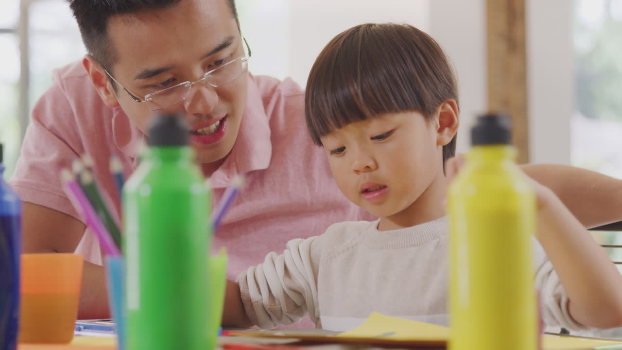 아시안 아버지 가 아들 과 함께 집 에서 테이블 위 에서 공예 를 하고 있다