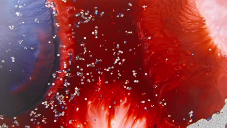 red and navy blue ink mixing in water with sparkling glitter, creating a cosmic nebula effect