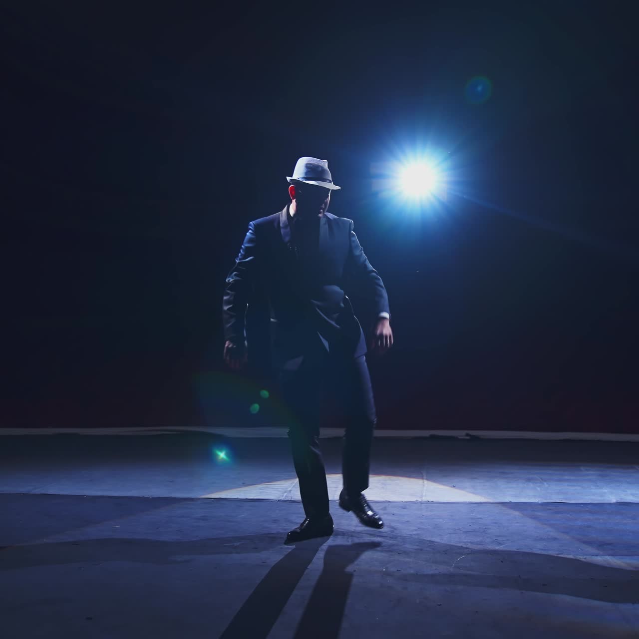 Senior man in costume on stage in darkness. Active man in hat dancing on stage during the performance in the theater.