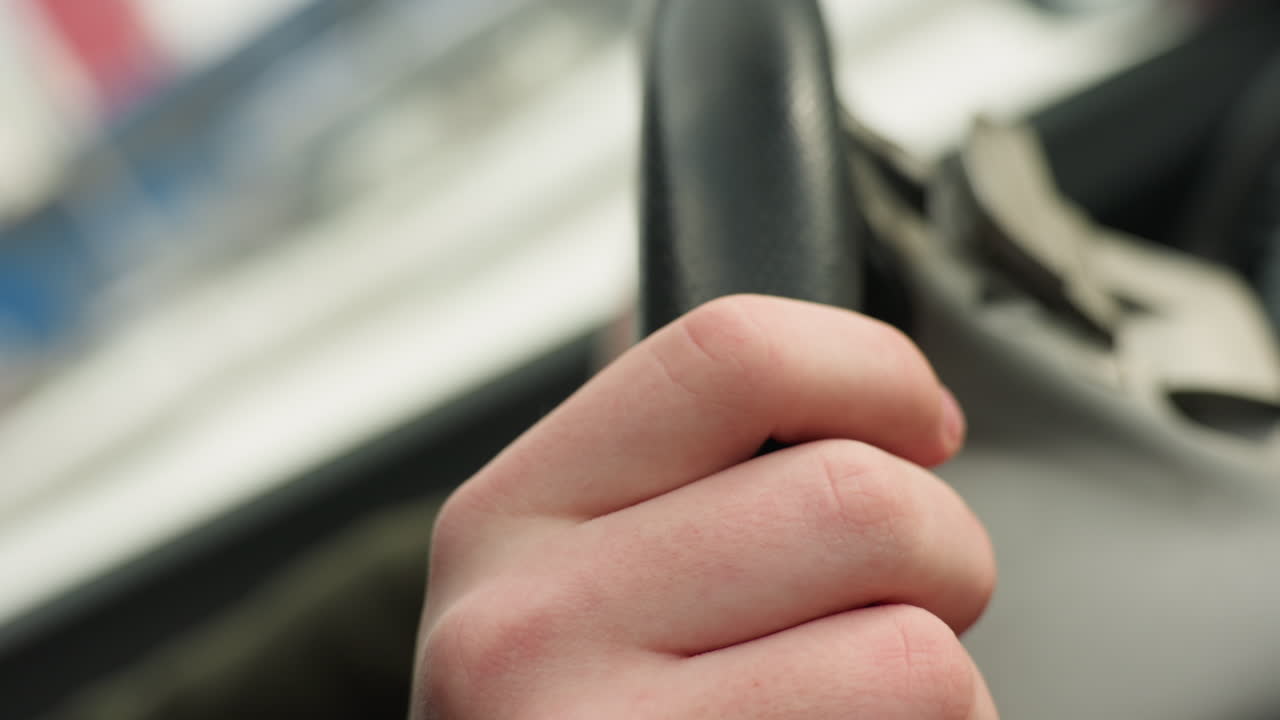 close up of fair skin hand gently tapping steering wheel with finger while holding it during daytime inside car with blurred abstract background through window