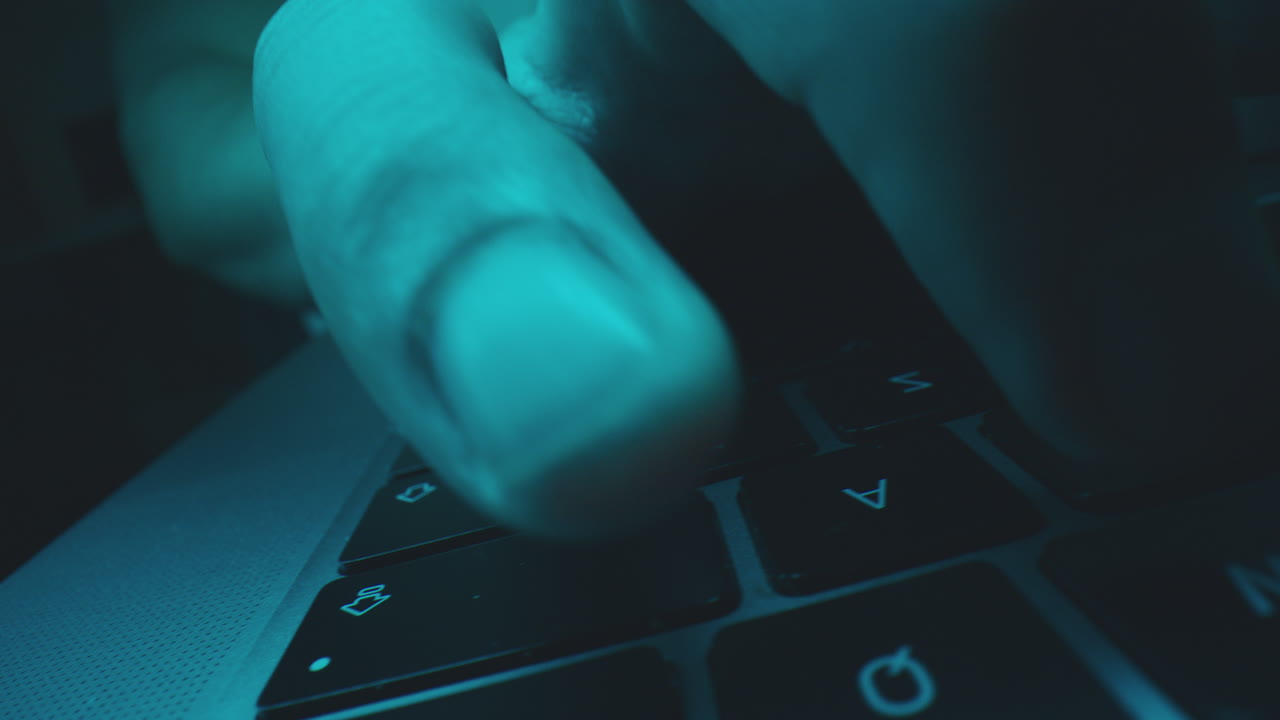 Hands typing on a laptop keyboard in the dark