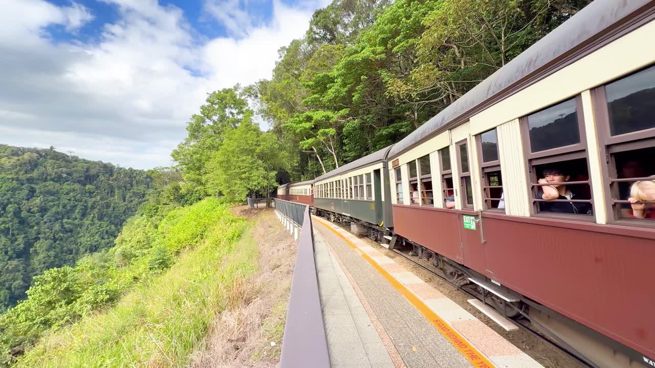Historic train moves along forested mountain track, bright daylight, scenic journey, passengers enjoying views