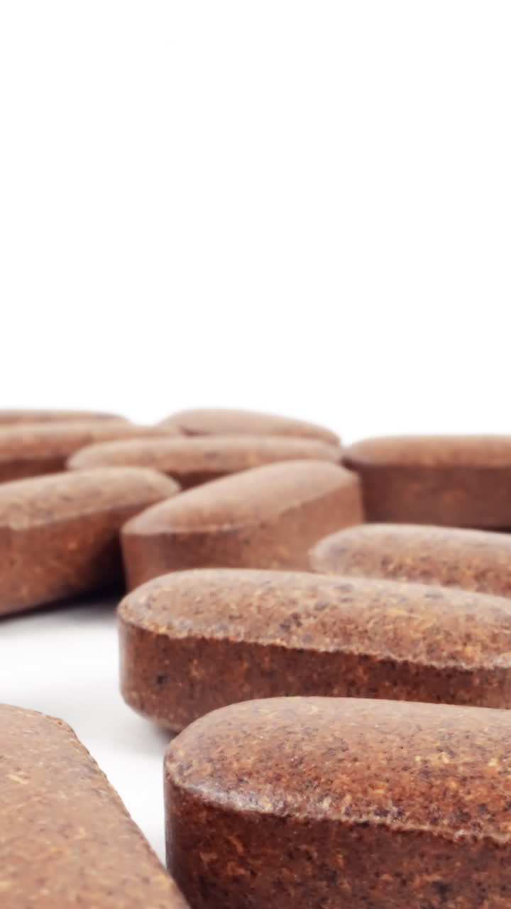 una serie de comprimidos de suplementos de hierbas marrones esparcidos sobre una superficie blanca