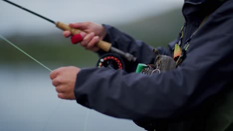 primer plano lateral del equipo y las manos de un hombre irreconocible pescando con la mosca