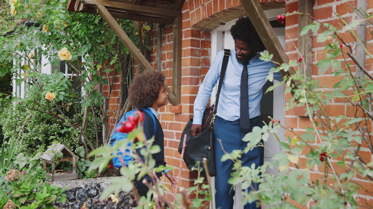 Smartly dressed middle aged black man and his pre teen son in school uniform leaving their house in the morning, exterior view, close up