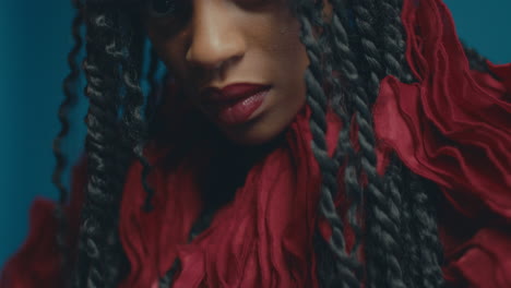 artistic black woman with braided hair bushes back long strands wearing fluffy red ruffled dress as light dances across body