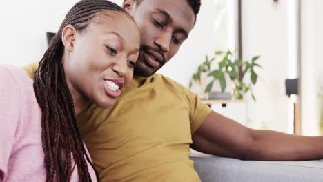 Glückliches-Afroamerikanisches-Paar,-Das-Tablet-Benutzt-Und-Zu-Hause-Auf-Der-Couch-Spricht,-In-Zeitlupe