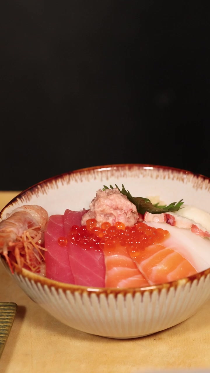 Primo piano di uno chef che guarnisce ciotole di frutti di mare freschi con wasabi e foglie di shiso.