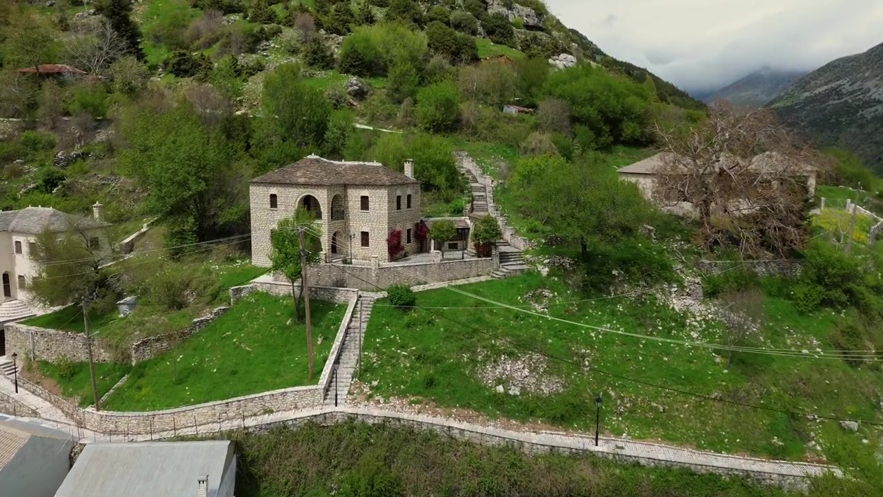 Avvicinamento cinematografico con drone 4K in volo verso il villaggio in pietra di Syrrako, salendo per rivelare la maestosa cima della montagna dietro. Paesaggio suggestivo e architettura tradizionale dell'Epiro.
