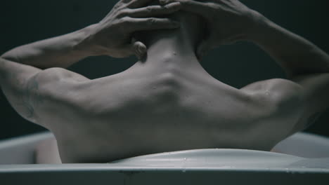 pale bald skinny man takes a bath in the creepy old bathroom at night